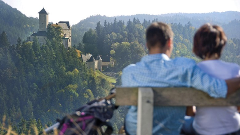 Youth camp site Rappottenstein, © Waldviertel Tourismus A couple sits on a bench with a view of a castle in a wooded landscape.