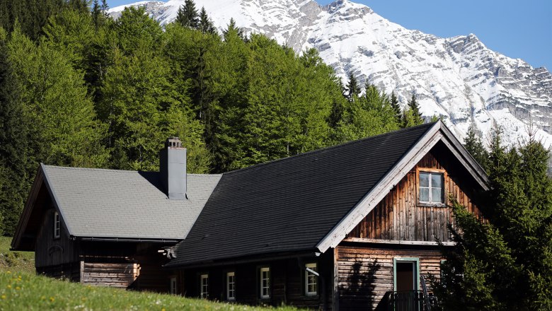 Wooden hut in front of a snow-covered mountain and green forest.