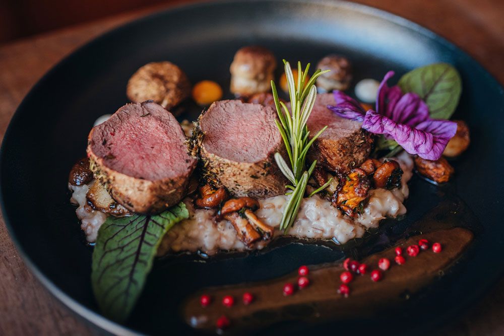 Pink roasted venison steak on risotto decorated with rosemary and flowers.