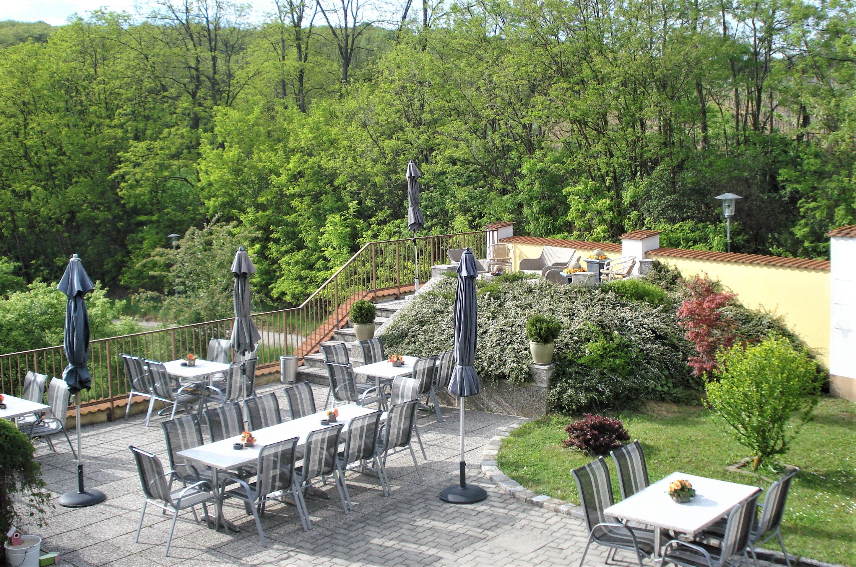 Guest terrace with tables, chairs and parasols, surrounded by green vegetation.
