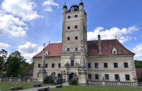 Greillenstein Castle with tower and red roof against a blue sky.