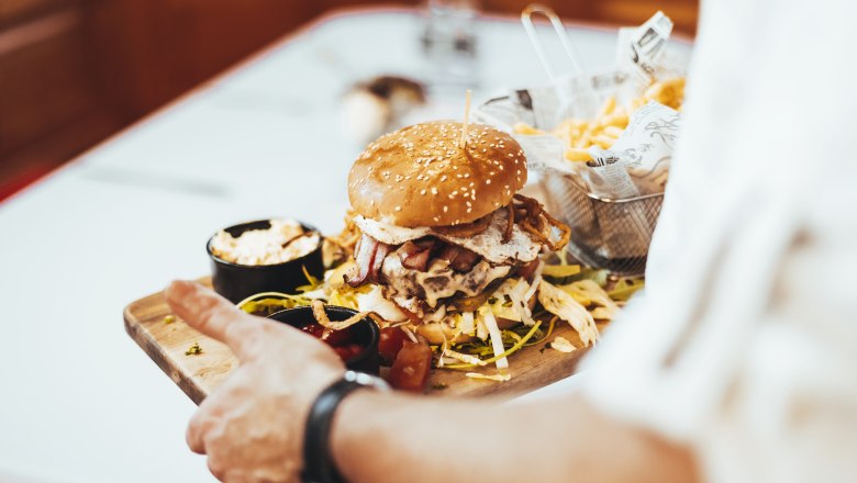 A burger with a sesame bun, bacon and fried egg on a wooden board, served with chips and dips.