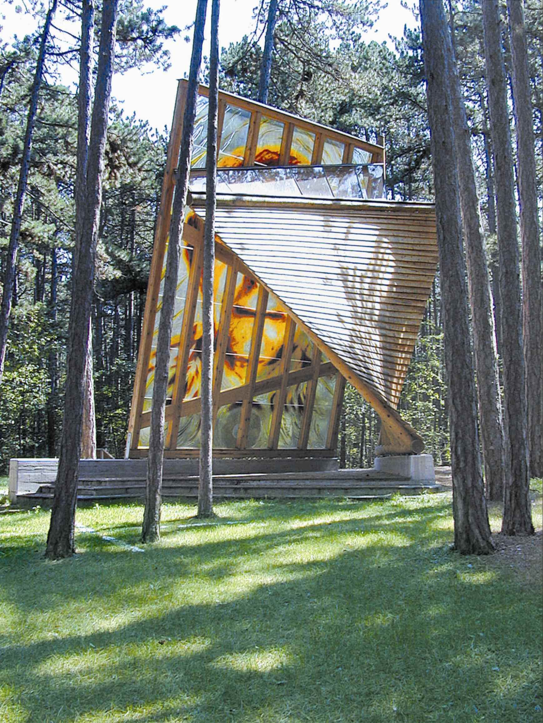 Modern wooden building in the forest with slanted glass windows.