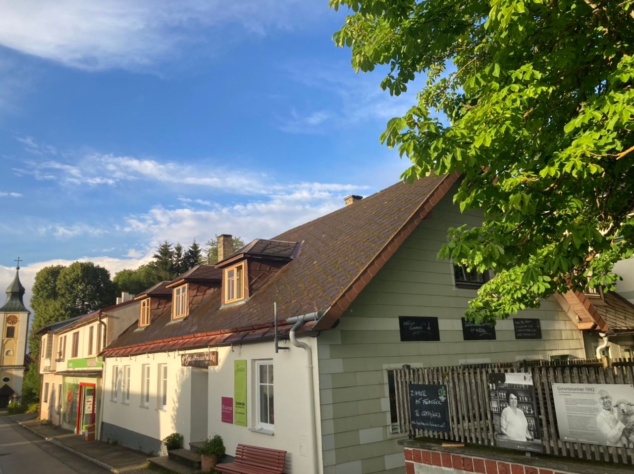 Exterior view of a traditional inn with a shingle roof and green façade, surrounded by trees and blue sky.