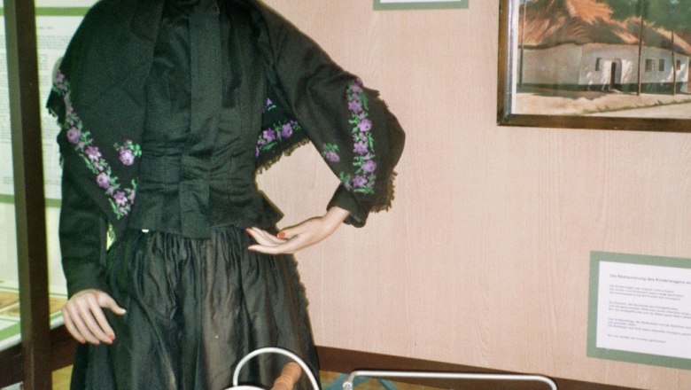 A mannequin in traditional clothing next to an old baby carriage in a showroom.