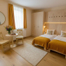 A cozy hotel room with two single beds, yellow curtains and a small table with flowers.