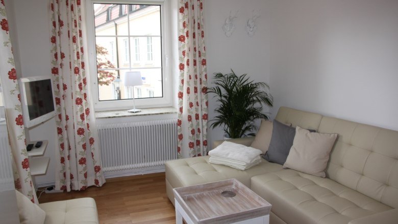 Bright living room with beige sofa, cushions, coffee table and window with curtains.
