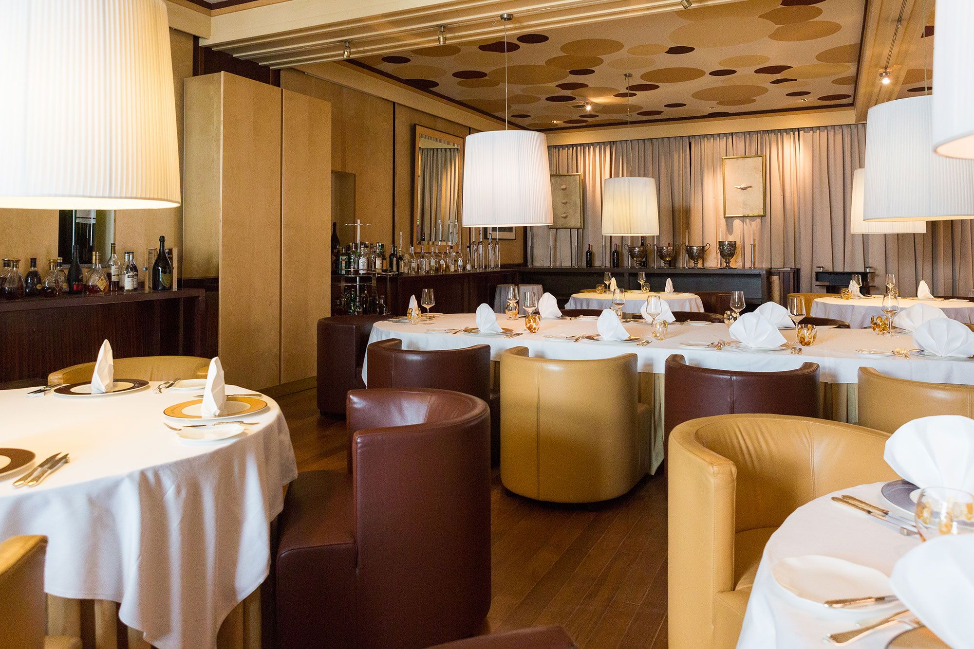 Elegant dining room with round tables, white tablecloths and brown and beige armchairs.