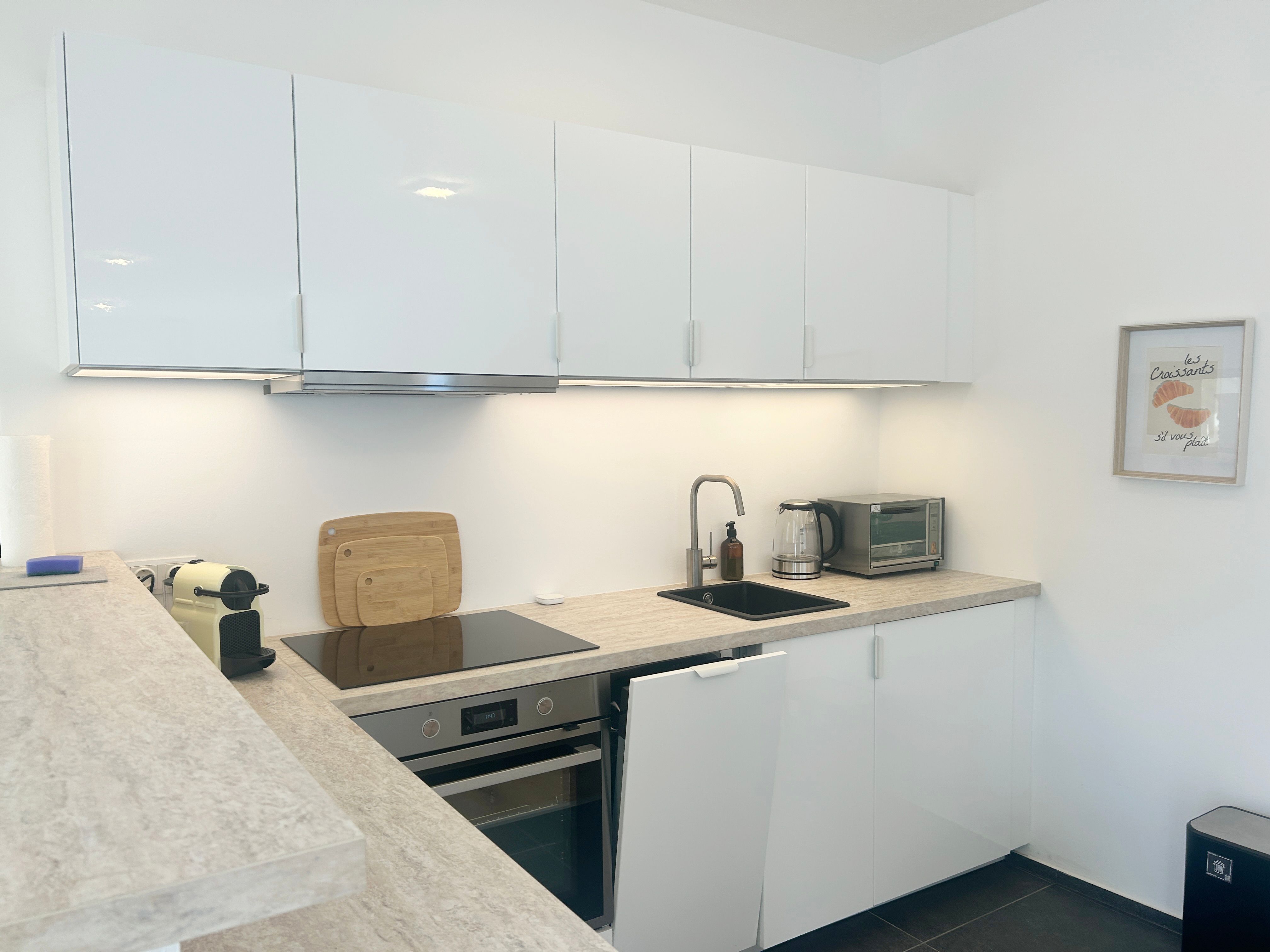 Modern kitchen with white cupboards, stove, sink and coffee machine.