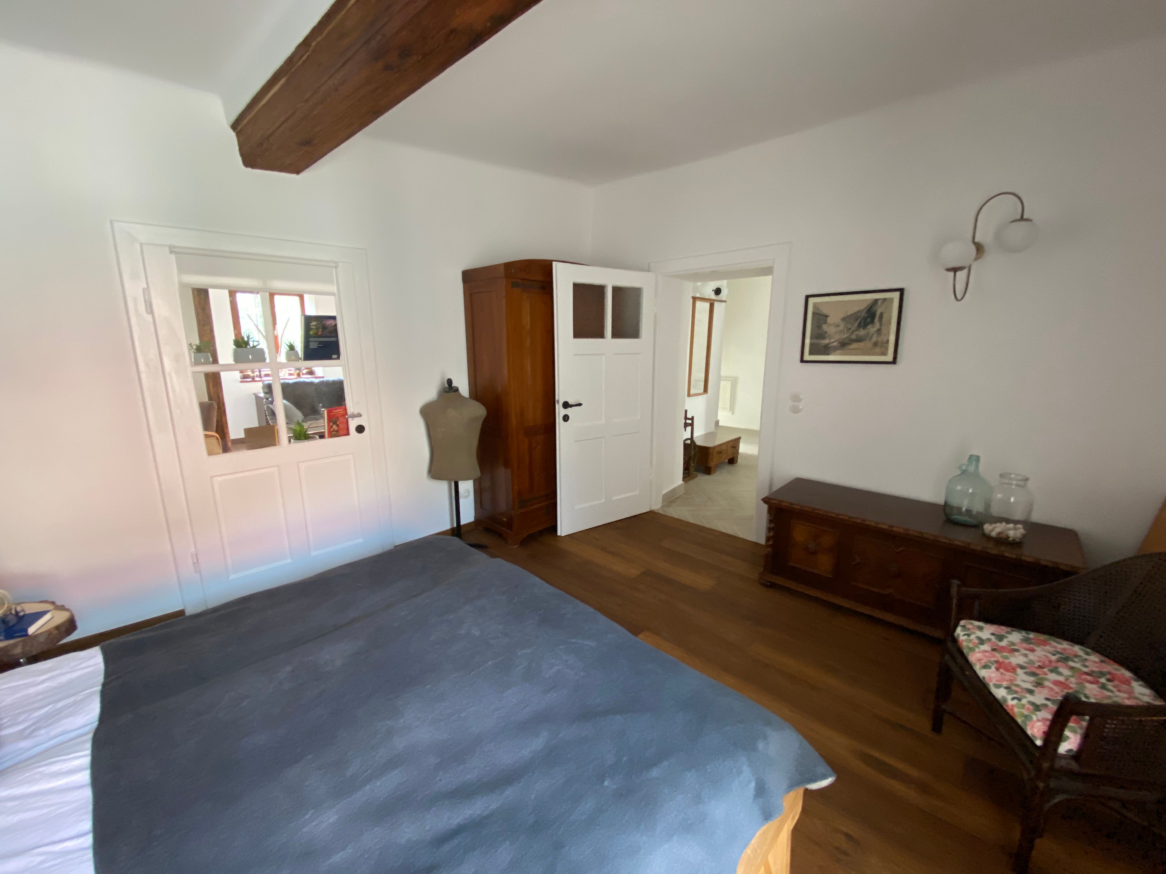 Bedroom with wooden floor, bed, closet, chest of drawers and chair.