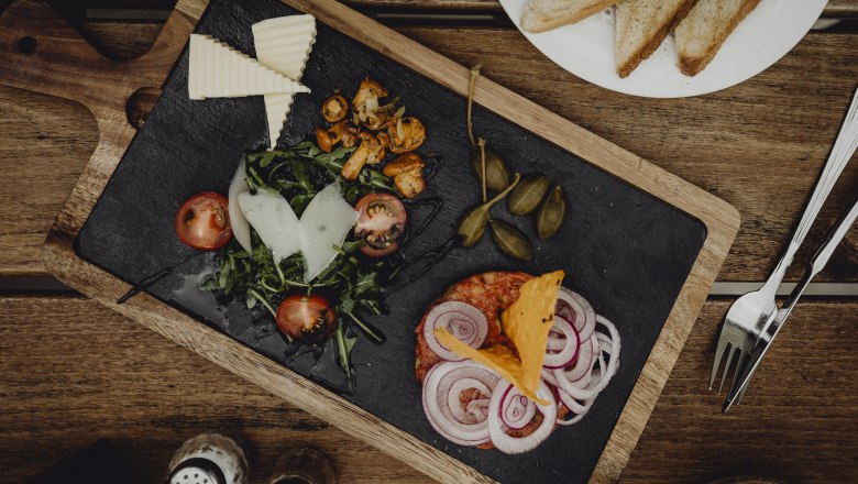 Appetizer platter with cheese, lettuce, tomatoes, onions and capers on a wooden board.
