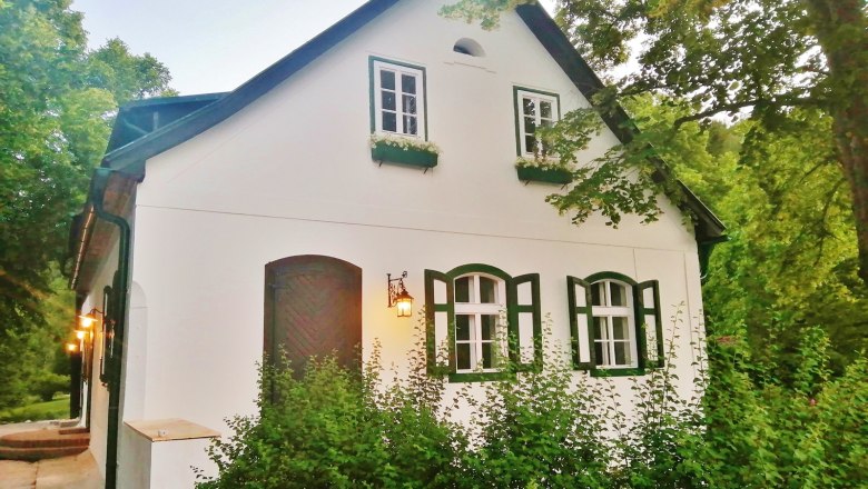 White house with green shutters, surrounded by trees.