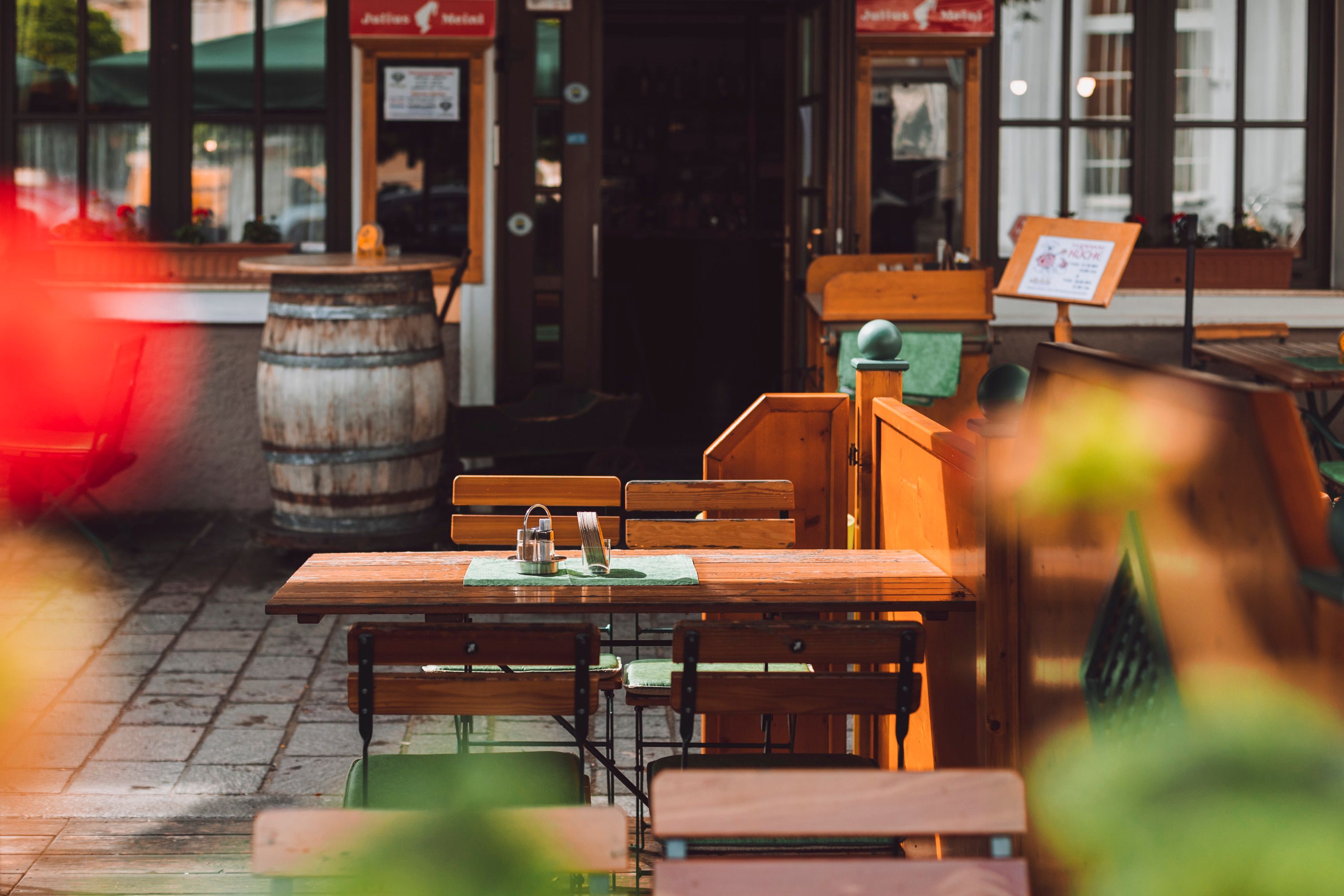 An empty table with wooden chairs in a guest garden, in the background a wine barrel and an entrance.