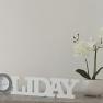 Decoration with 'HOLIDAY' lettering and white orchid in a pot on a table.