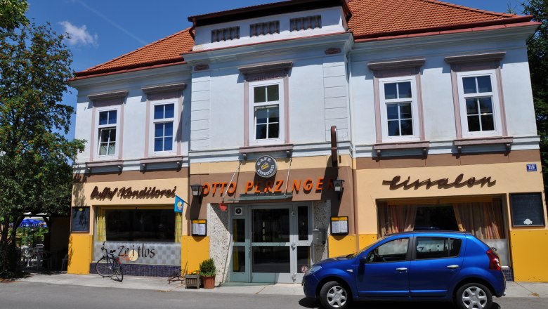 Exterior view of a café with a blue façade and red roof, a blue car parked in front of it.