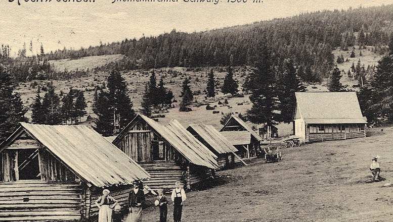 Historical photograph of wooden huts on the Mönichkirchner Schwaig, surrounded by forest and meadows, with people in the foreground.