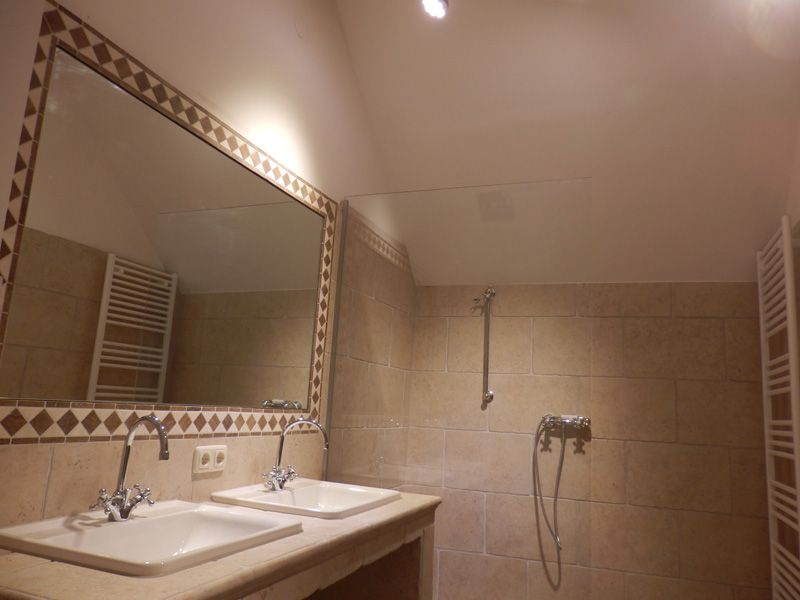 Bathroom with two washbasins, large mirror and beige tiled wall.