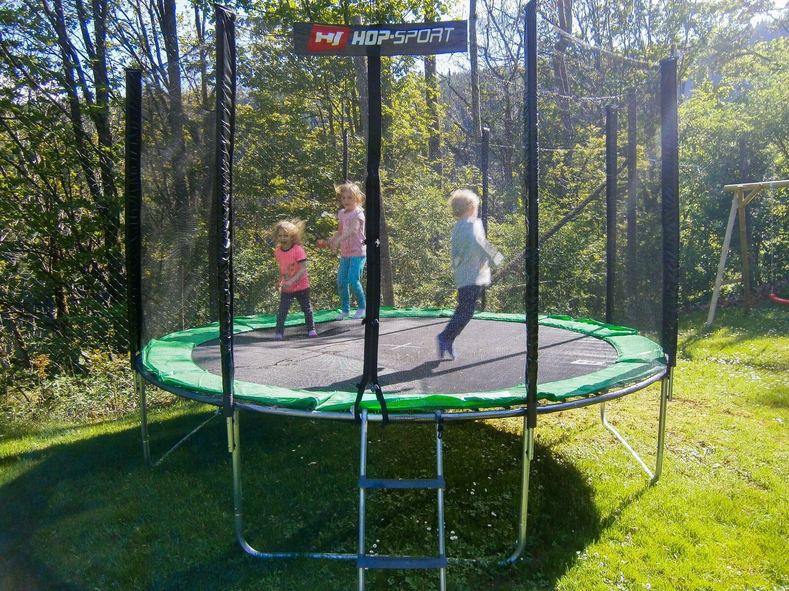 Three children jumping on a trampoline outdoors.