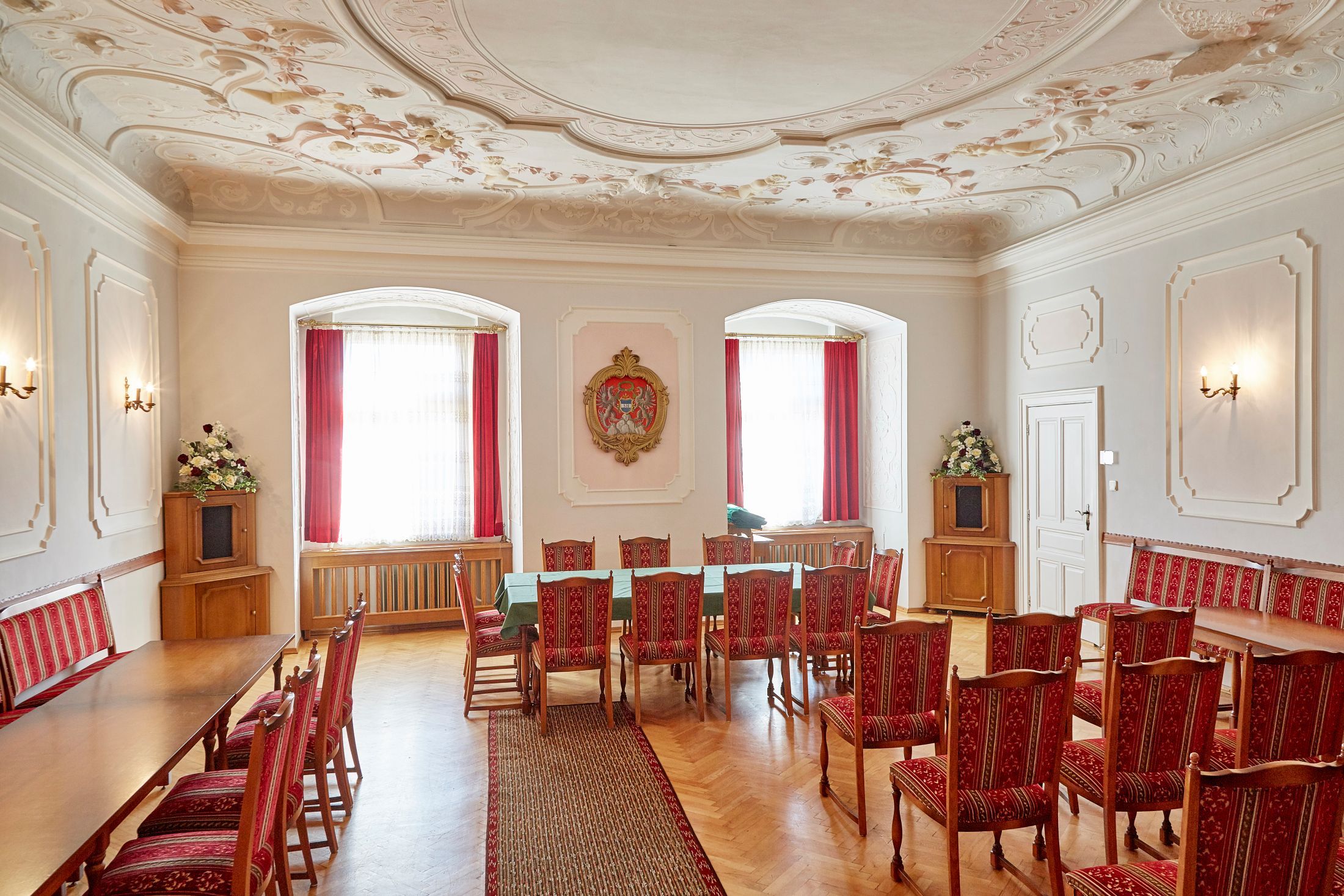An elegant room in Groß Siegharts Castle with red chairs, a long table and a decorative ceiling.