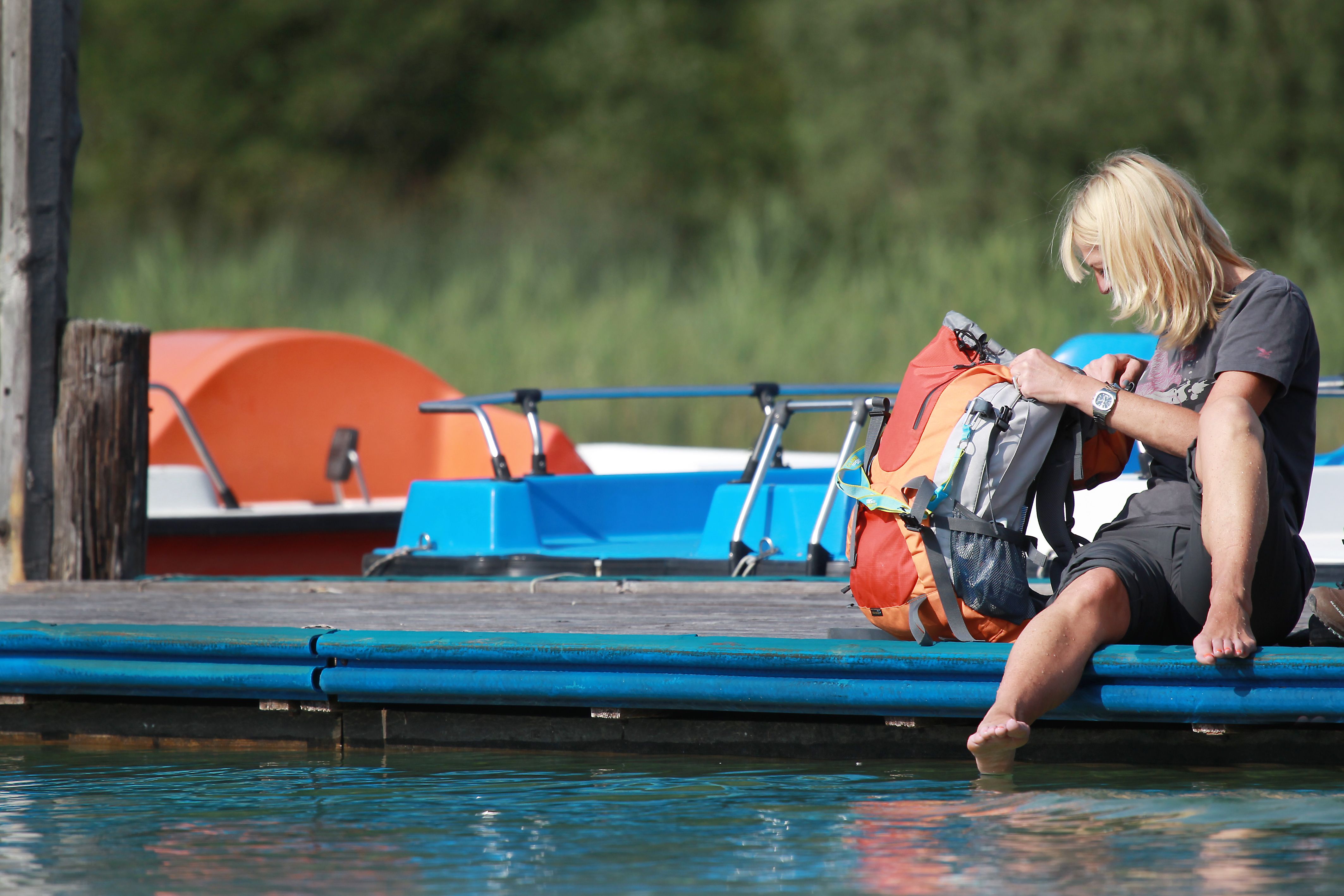 Person sitting on a jetty on Lake Erlaufsee with their feet in the water, next to a rucksack. Pedal boats can be seen in the background.