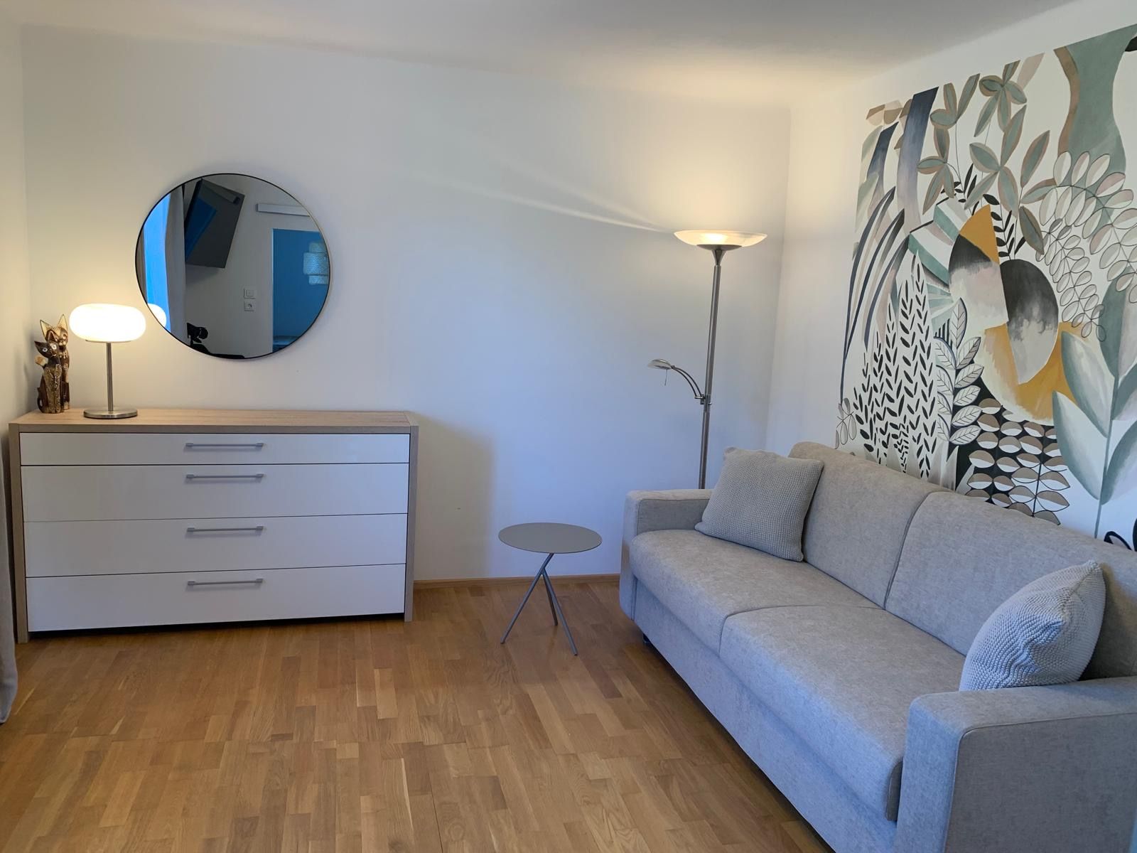 Modern living room with gray sofa, chest of drawers, mirror and decorative wall art.