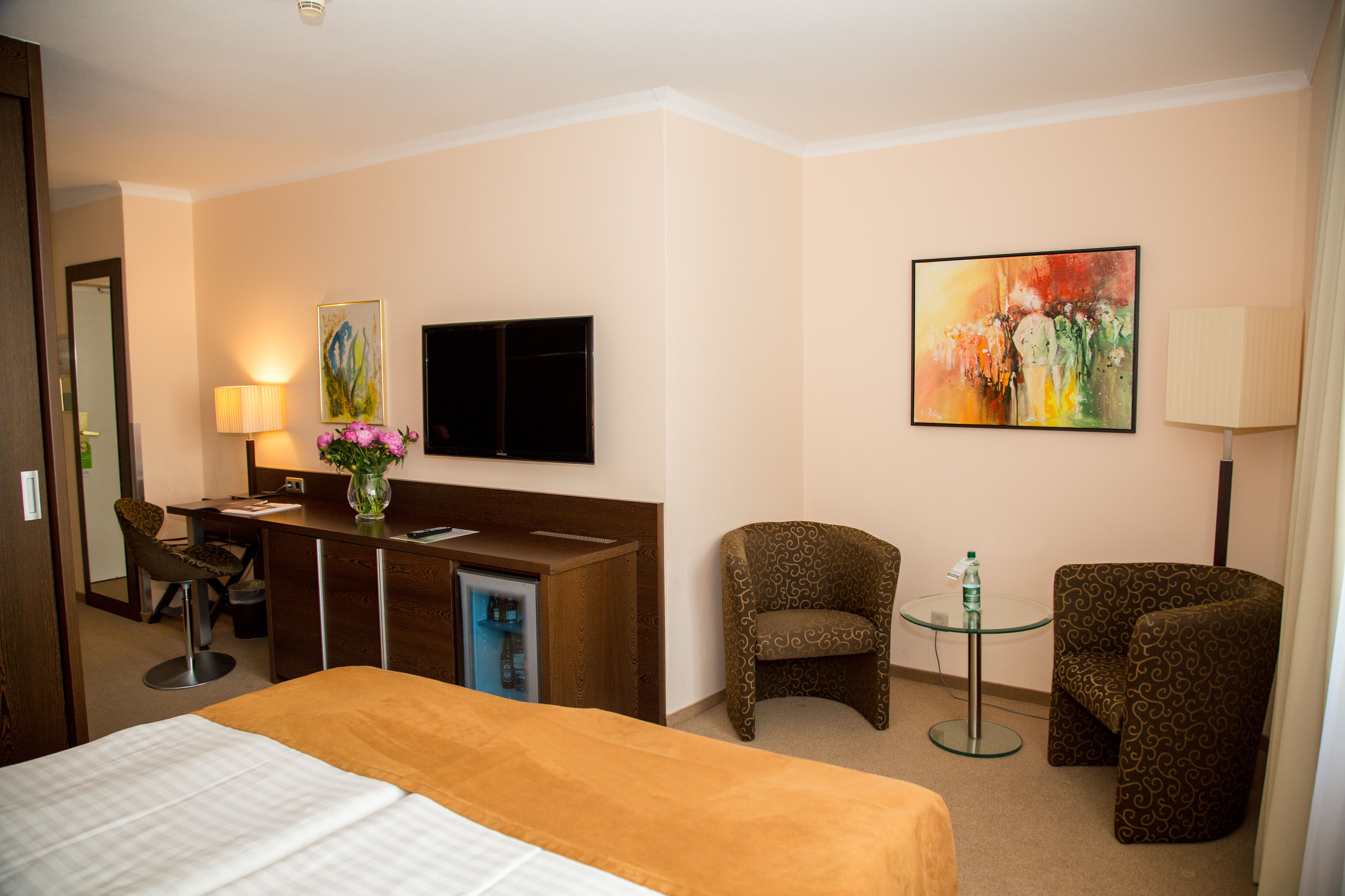 Hotel room with double bed, desk, TV and two armchairs.