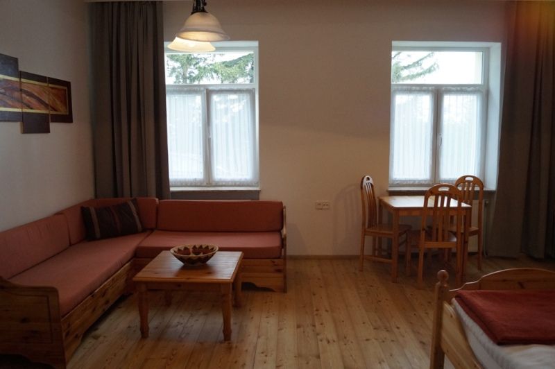 Cozy room with wooden furniture, sofa, table and chairs, two windows and a picture on the wall.