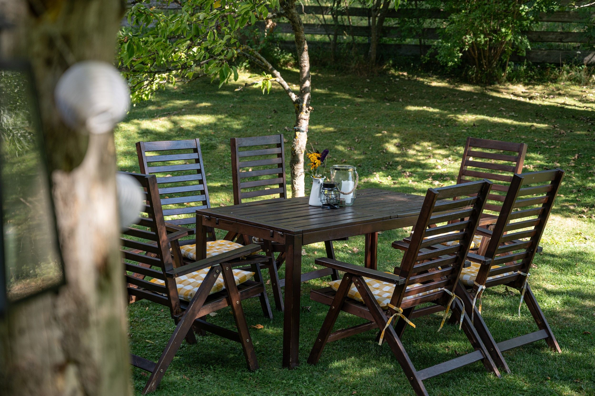 Garden with wooden table and chairs, decorated with flowers and candles.