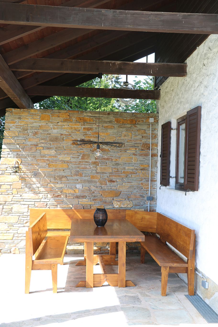 Wooden seating area under a covered area with a stone wall in the background.