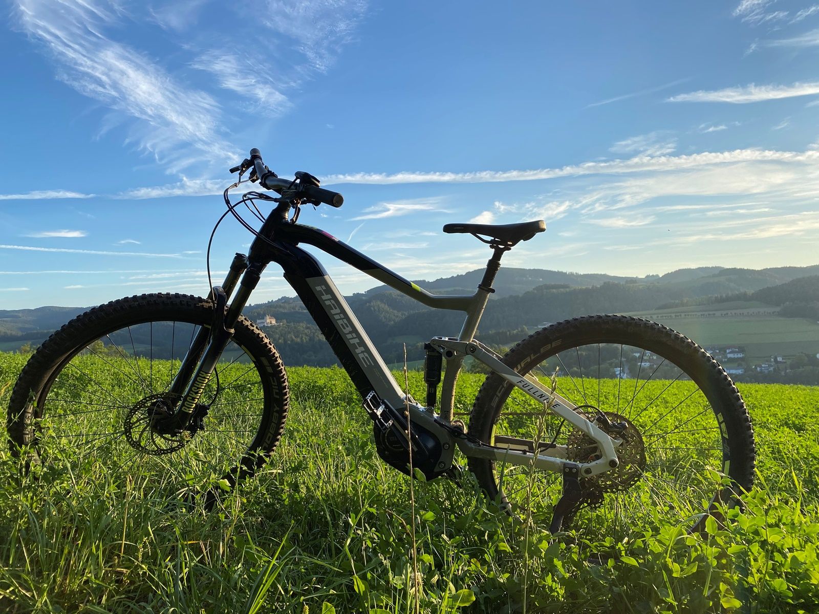Close-up of a bicycle on a green meadow with a hilly landscape in the background.