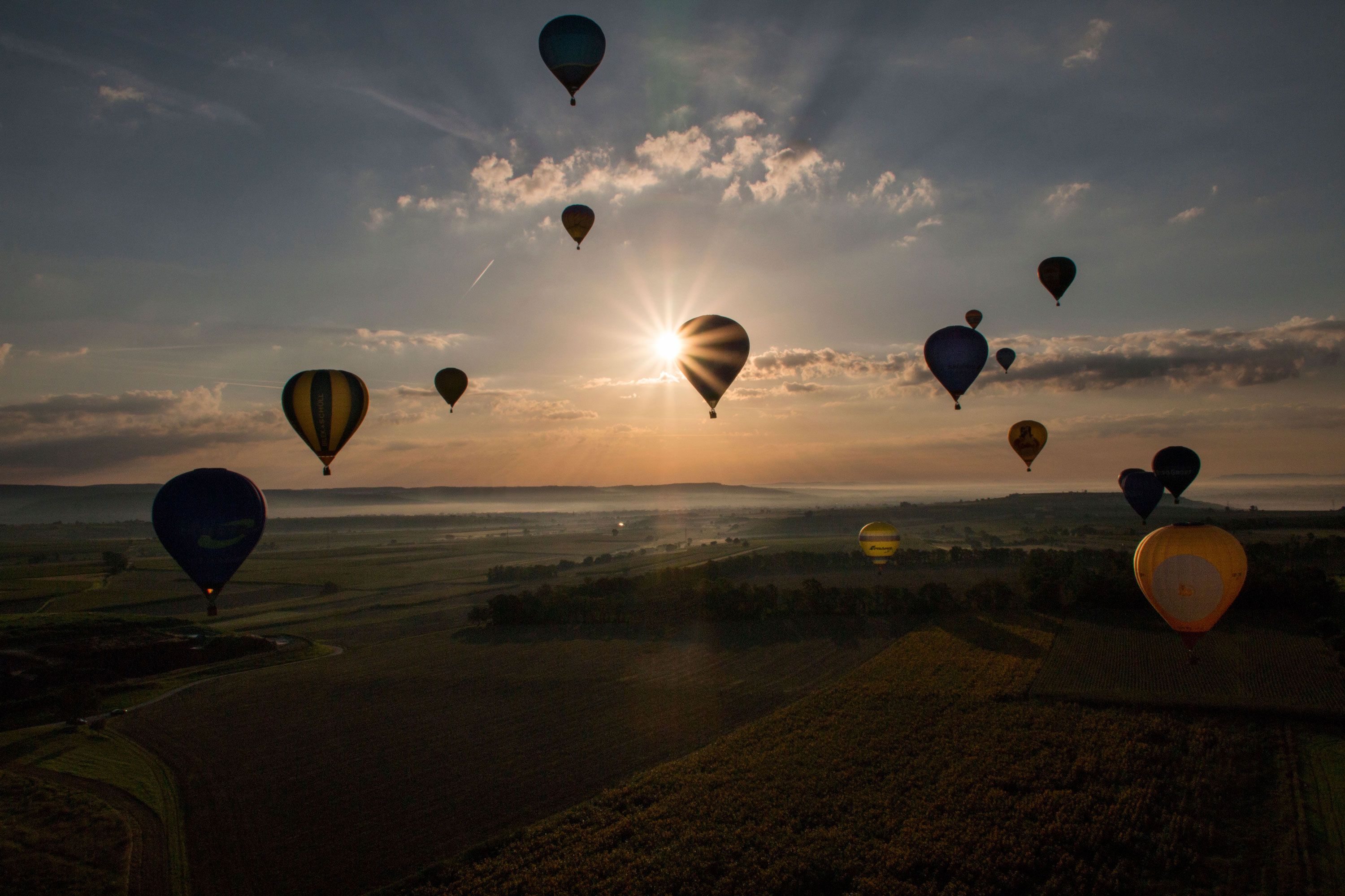 Hot air balloons float over a landscape at sunrise.