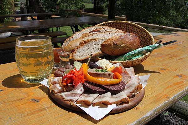 Board snack with bread, sausage, bacon and drinks on a wooden table outside.