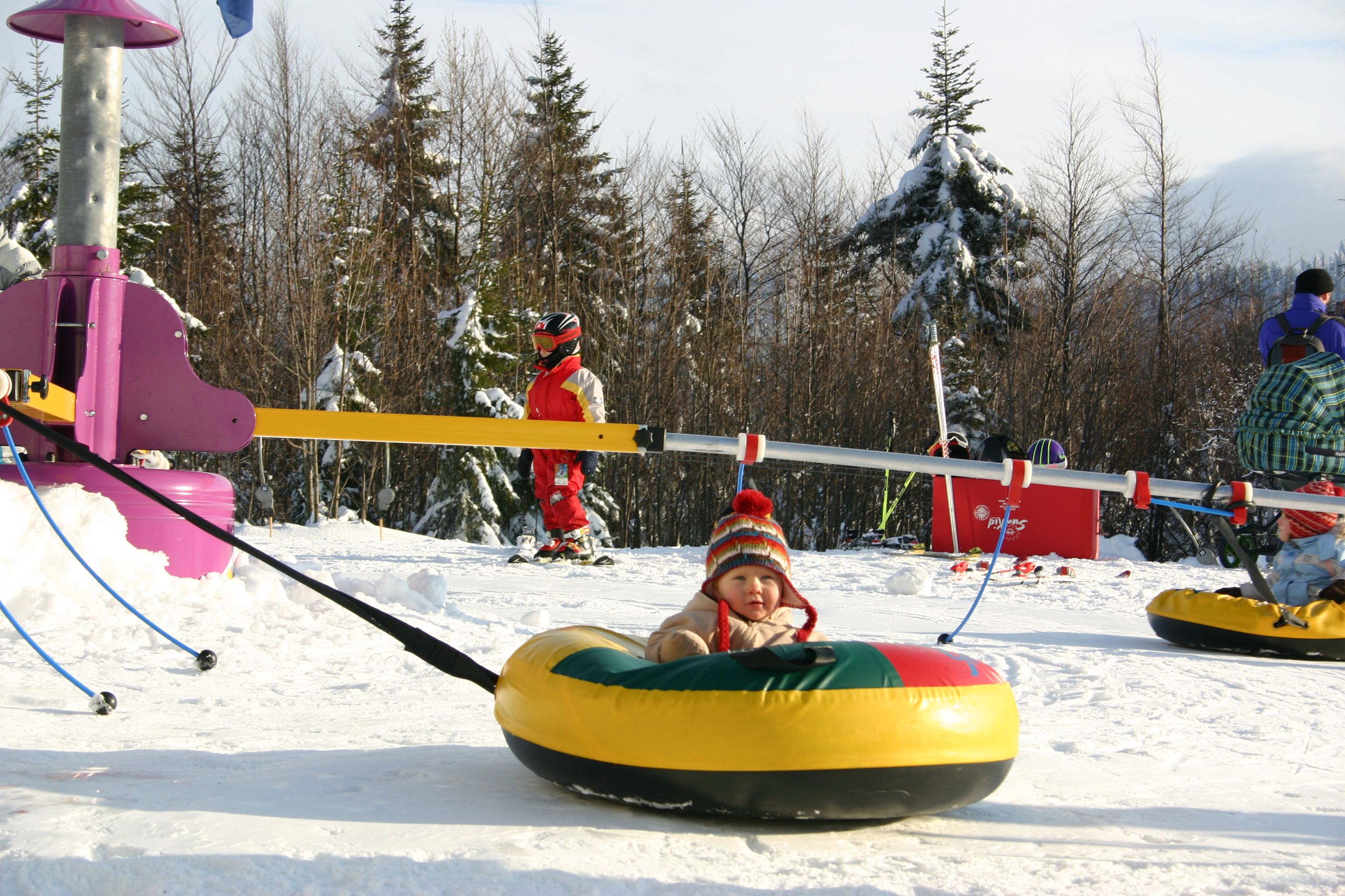 Toddler in a colorful snow tire on a snowy hill with other children in the background.