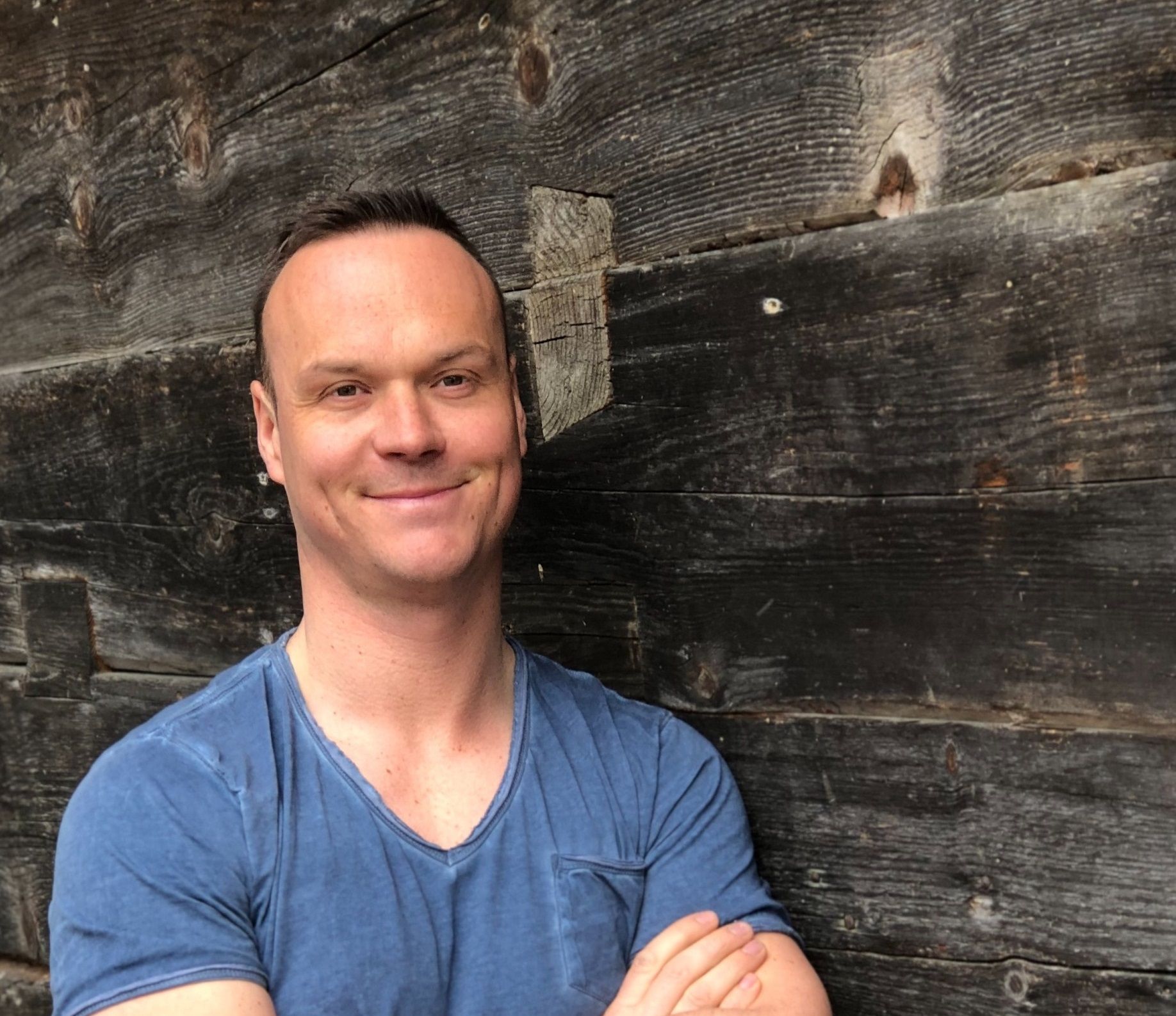 Man in blue T-shirt in front of wooden wall.