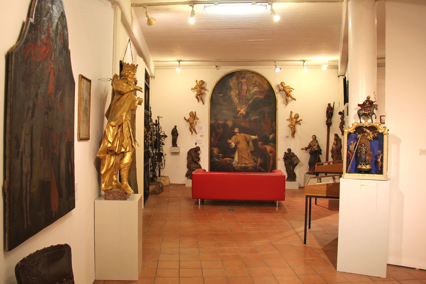 Interior view of a museum with sculptures and paintings, red sofa in the center.