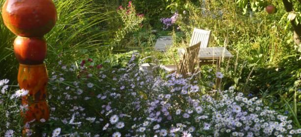 A blooming garden with purple flowers, a wooden table and chairs in the background.