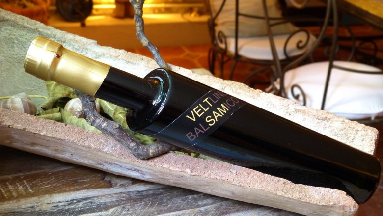 A black vinegar bottle with a golden cap lies in a rustic wooden bowl.