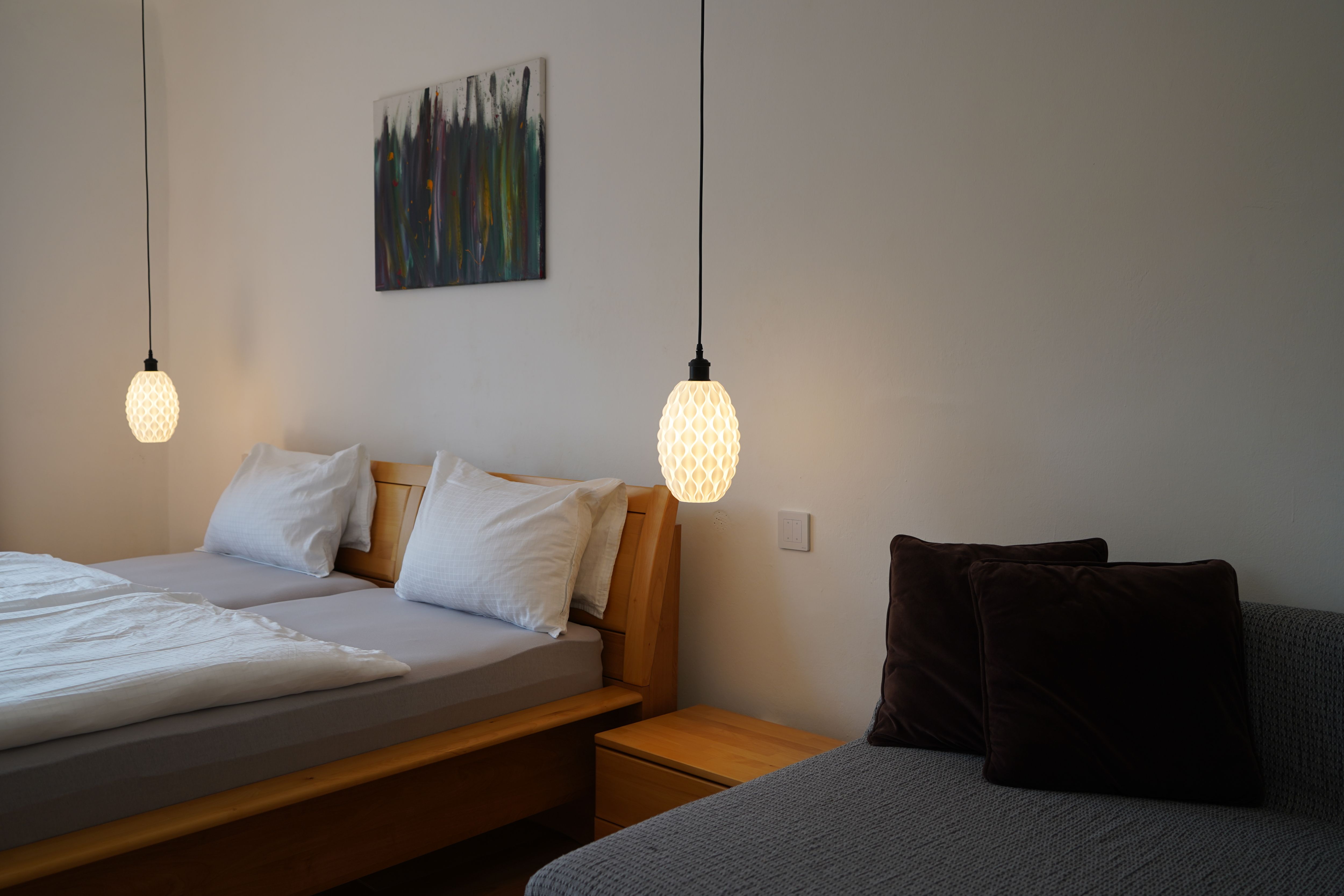 Bedroom with double bed, two hanging lamps and a sofa with cushions.