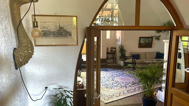 Interior view of a living room with plants, a sofa and a decorative wall object in the shape of a bird with a lamp.