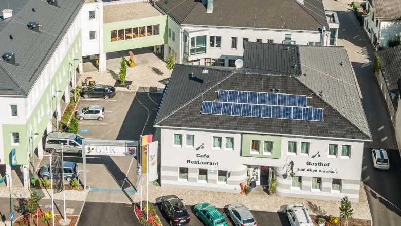 Aerial view of a building complex with the Gasthof zum Alten Brauhaus, solar panels on the roof and several parked cars.