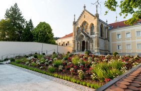 A church with Gothic elements and a well-tended garden full of flowers in the foreground.