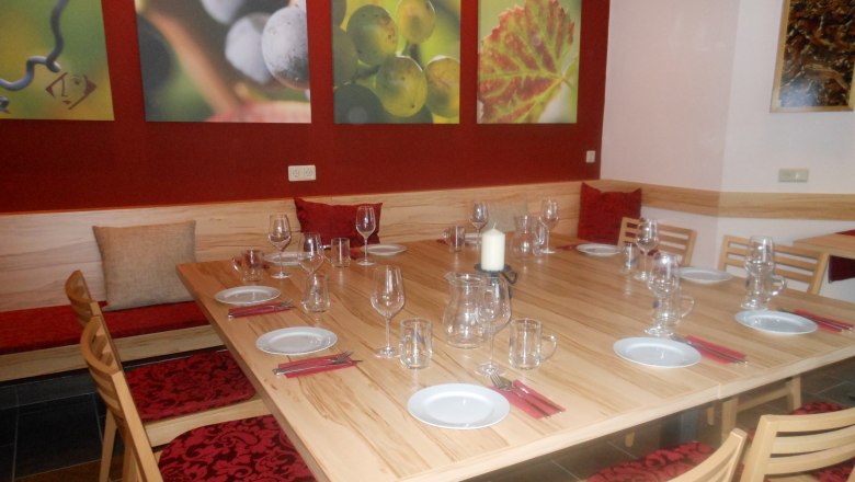 A tasting room with a covered wooden table, wine glasses and murals of grapes.
