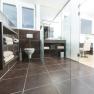 Modern bathroom with dark tiles, glass walls and white sanitary facilities.
