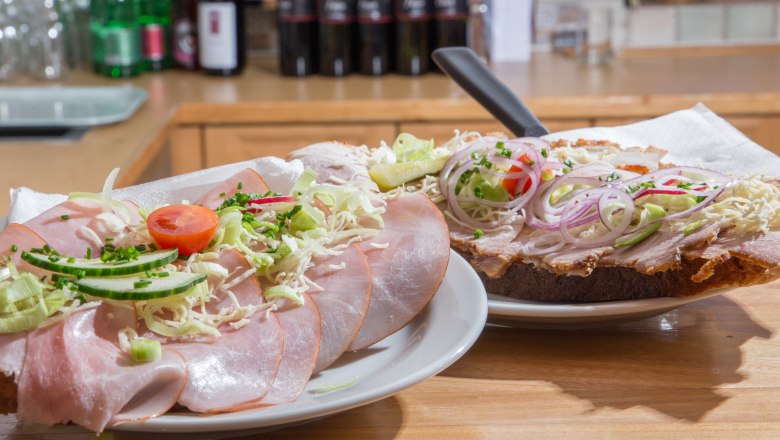 Two sandwiches with ham, onions and vegetables on a wooden table.