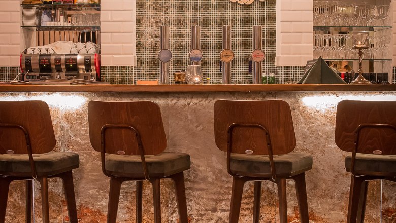 Interior view of a stylish bar with wooden chairs and illuminated counter.