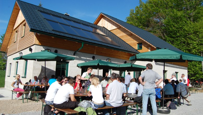 People sit at tables in front of a hut with solar panels and parasols.