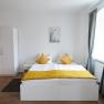 Modern double room with white bed, yellow pillows and gray curtains.