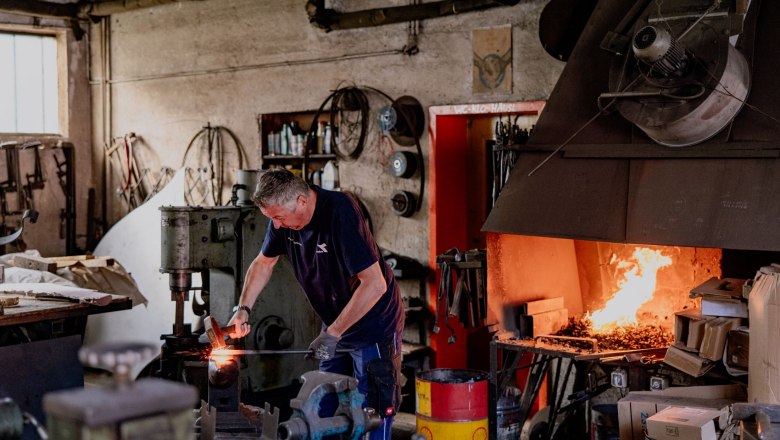 A blacksmith works in a workshop with a burning forge fire.
