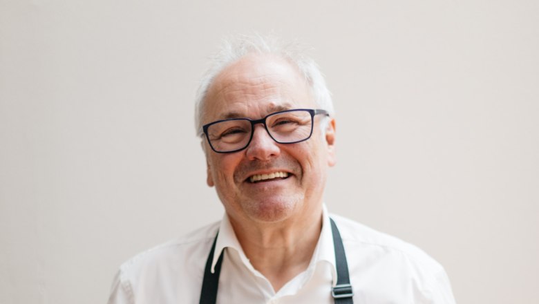 A smiling man in an apron holds a plate of food.