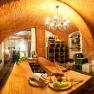 A cozy wine cellar with brick walls, a wooden table, shelves of wine bottles and a plate of cheese and grapes.